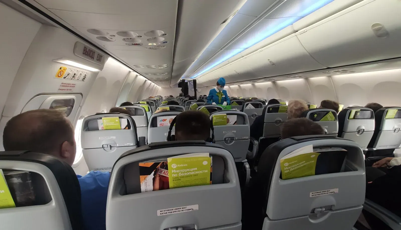 Салон A321 S7 в полёте: бортпроводник в проходе, зелёные инструкции в спинках