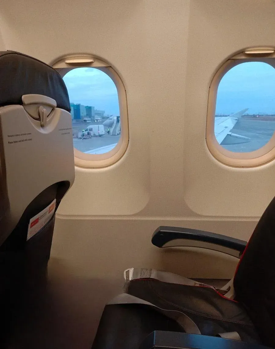 Место у иллюминатора в экономе A319 «Уральских авиалиний», вид на перрон перед вылетом