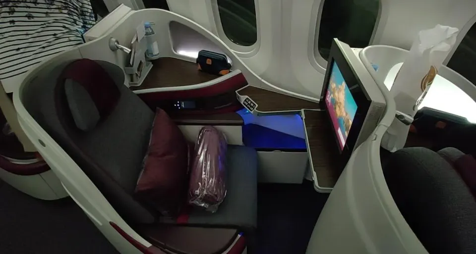 Кресло бизнеса Boeing 787-8 Qatar Airways у окна с подушкой и пледом в упаковке