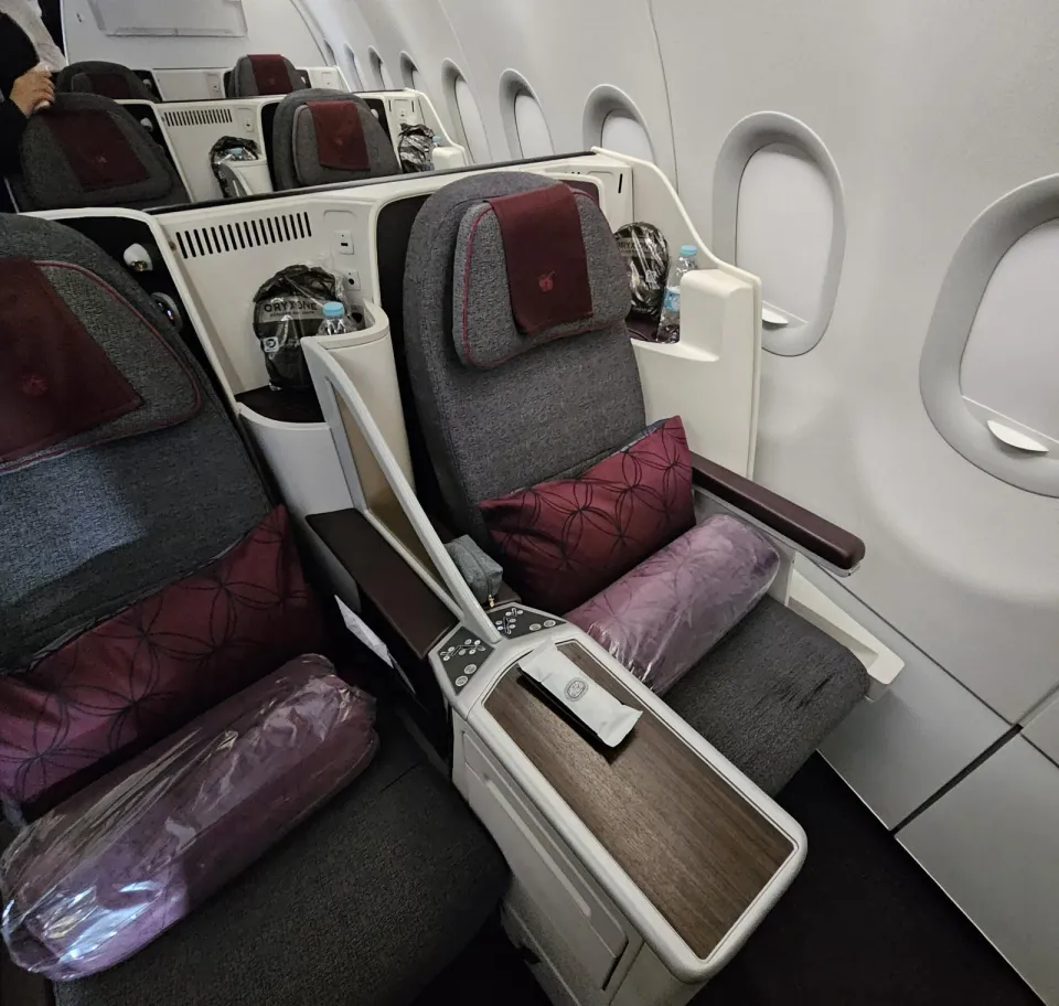 Кресло бизнеса Qatar Airways на A320 у окна: серая обивка и бордовая подушка